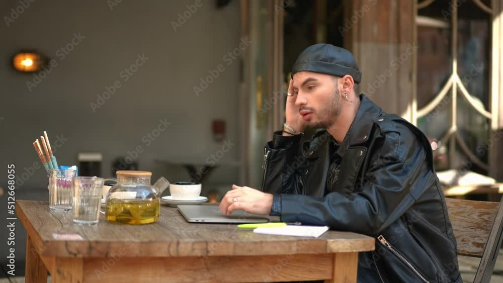 Side view young Caucasian gay man closing laptop sighing looking away sitting in outdoor cafe. Portrait of intelligent confident tired Caucasian LGBTQ freelancer working online in urban city Side view young Caucasian gay man closing laptop sighing looking away sitting in outdoor cafe. Portrait of intelligent confident tired Caucasian LGBTQ freelancer working online in urban city