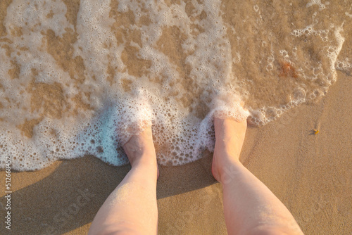 Fototapeta Naklejka Na Ścianę i Meble -  Female feet in the sand by the sea, covered with sea wave foam.