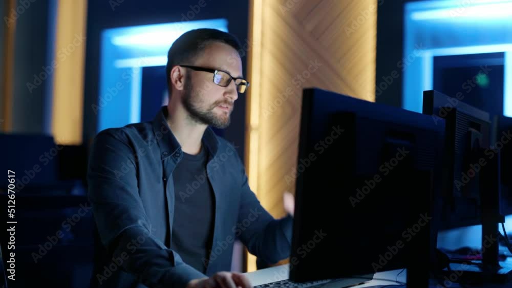 A man with glasses sits and thinks, typing on a computer in the office at night. A man with glasses sits and thinks, typing on a computer in the office at night.