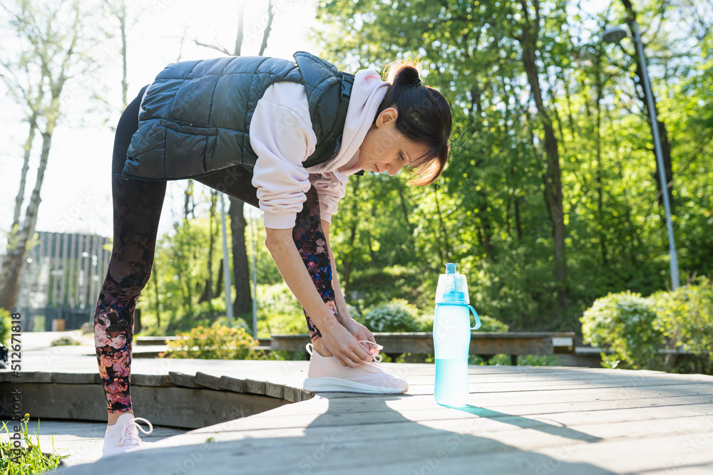 Woman tying running shoes in the park outdoor, female runner ready for jogging on the road outside Woman tying running shoes in the park outdoor, female runner ready for jogging on the road outside