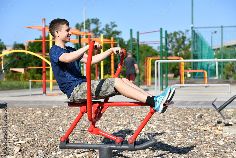Fototapeta premium a teenage boy trains on a sports ground outdoors, he does physical exercises, a healthy lifestyle, a bright sunny day in summer