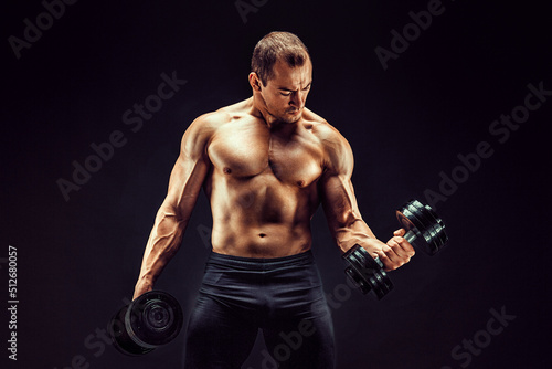 Powerful man doing the exercises with dumbbells. Photo of young man with good physique isolated on black background. 