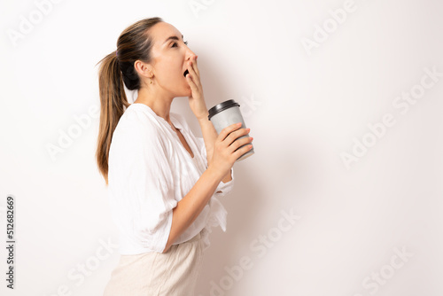 Image of young secretary tired woman wearing white casual shirt drinking coffee from paper cup in the office standing isolated over white background