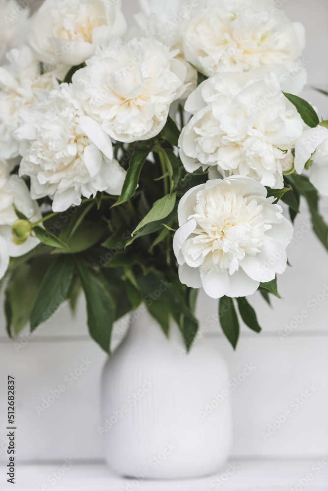 Beautiful white bouquet of peonies in a white vase on a white wooden background. Close-up. Flowers and buds.