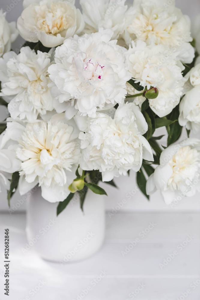 Beautiful white bouquet of peonies in a white vase on a white wooden background. Close-up. Flowers and buds. Beautiful white bouquet of peonies in a white vase on a white wooden background. Close-up. Flowers and buds.