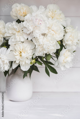 Beautiful white bouquet of peonies in a white vase on a white wooden background. Close-up. Flowers and buds.