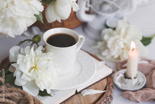 A beautiful postcard. A white coffee cup with a saucer, candles and a vase with a bouquet of white peonies. Beautiful still life. Spring, summer time. The concept of "Good morning".