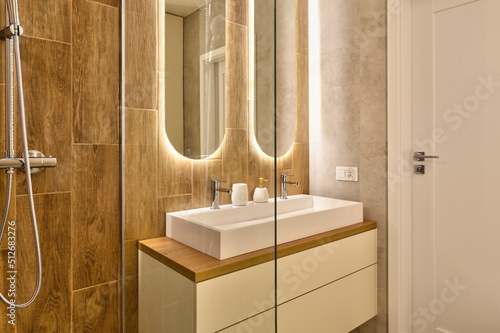 Fotografiet Interior of bathroom with ceramic washbasin with faucet, wooden tiles on the wall and modern bathtub for shower