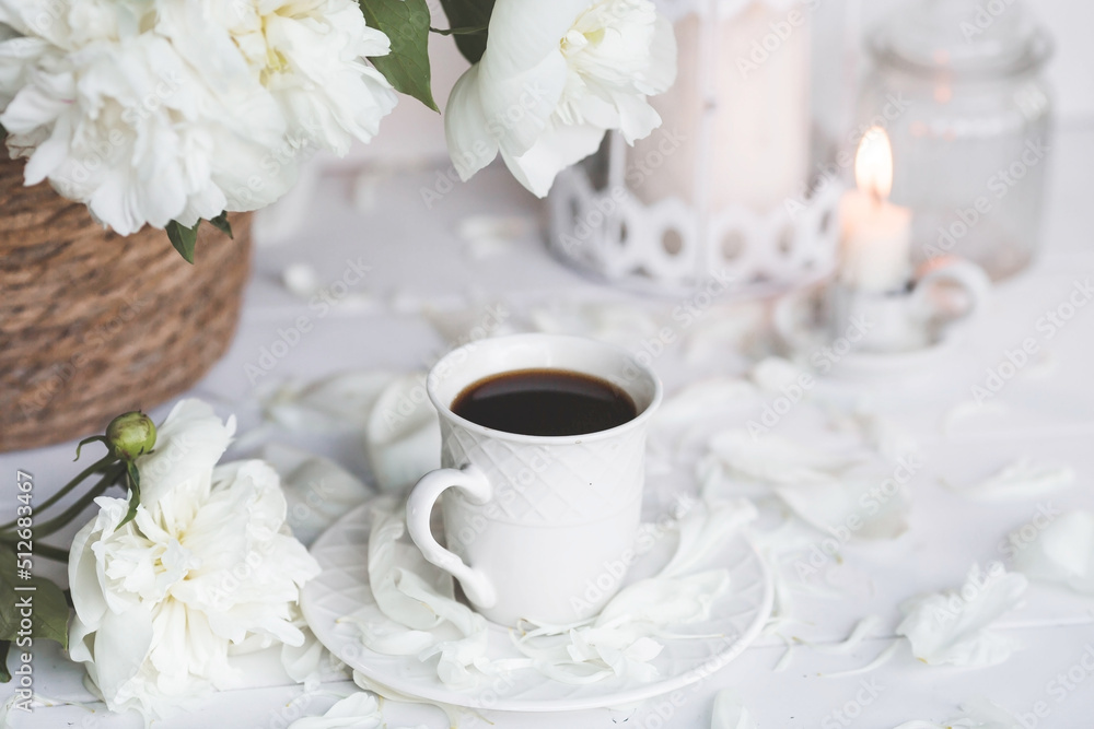 A beautiful postcard. A white coffee cup with a saucer, candles and a vase with a bouquet of white peonies. Beautiful still life. Spring, summer time. The concept of 