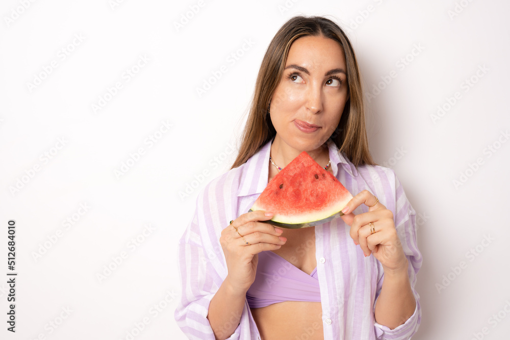 bikini Woman leaning against white background holding watermelon up to mouth