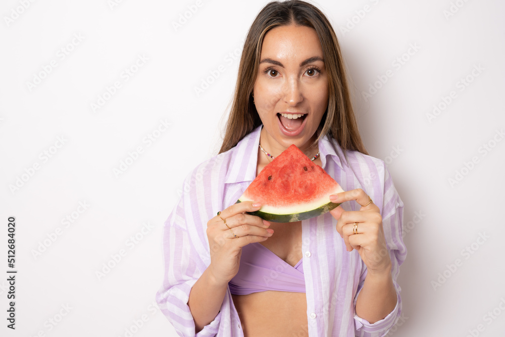 bikini Woman leaning against white background holding watermelon up to mouth