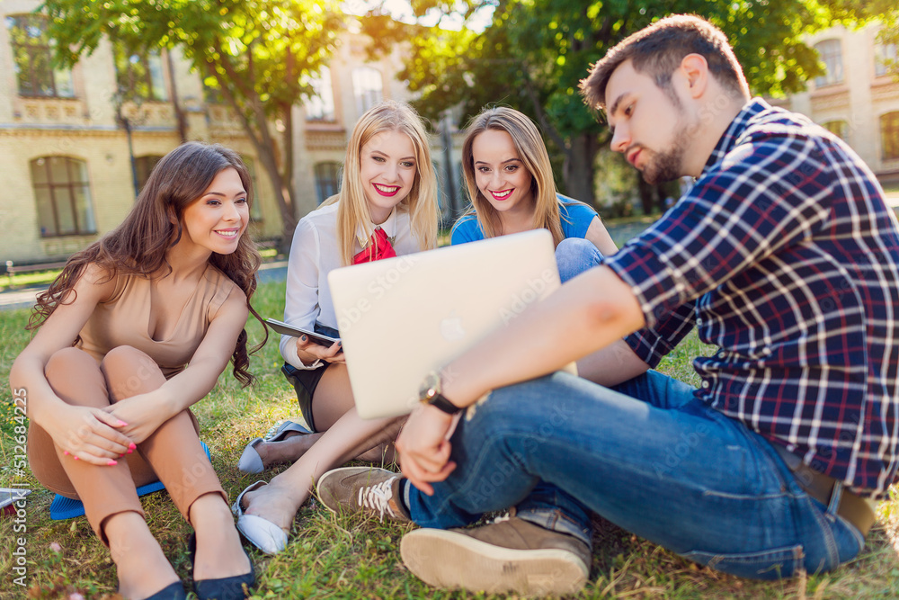 A group of cheerful students near the university building on the lawn with a laptop, books and notebooks
A group of cheerful students near the university building on the lawn with a laptop, books and notebooks