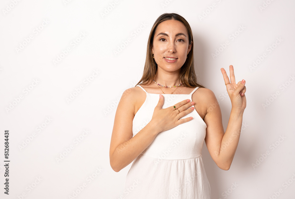 Happy brunette young woman in white dress isolated on white studio background hold hands on heart chest feel thankful, smiling grateful young female thanking god, show love, empathy and care Happy brunette young woman in white dress isolated on white studio background hold hands on heart chest feel thankful, smiling grateful young female thanking god, show love, empathy and care