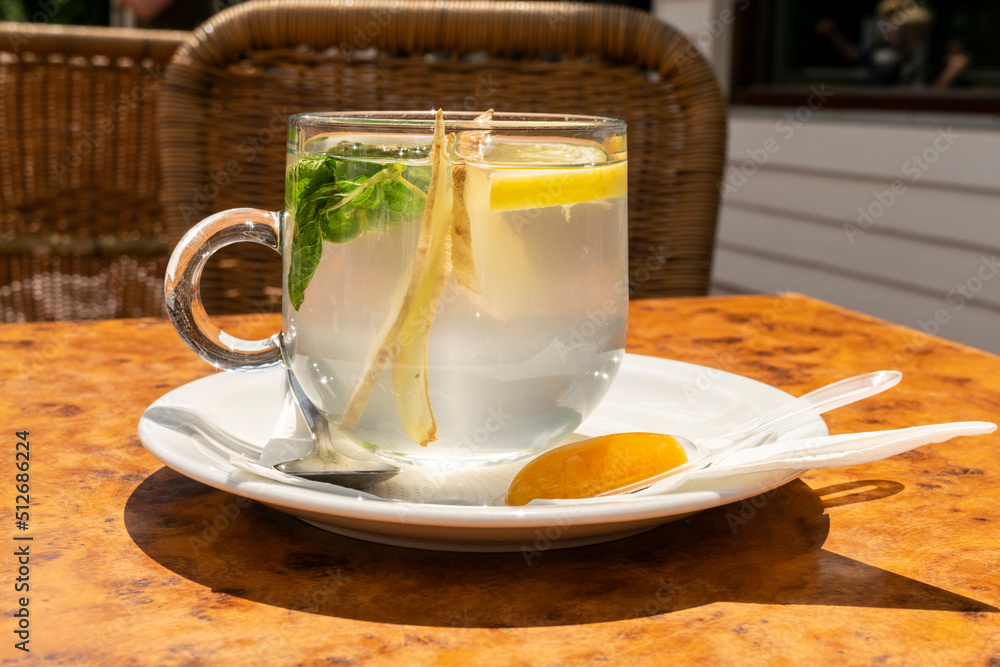 Mint tea with lemon, ginger and honey in a transparent glass cup close-up. Organic healthy herbal tea drink. Cozy cafe with wicker chairs. Mint tea with lemon, ginger and honey in a transparent glass cup close-up. Organic healthy herbal tea drink. Cozy cafe with wicker chairs.