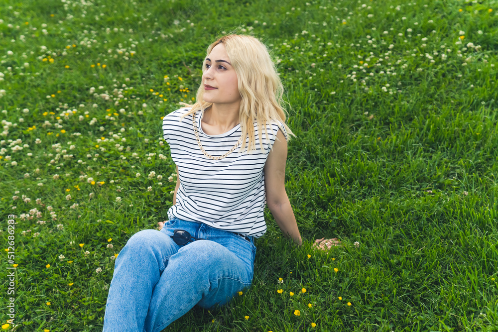 Fototapeta premium blond European girl sitting on the grass and looking up to the sky. medium full shot. High quality photo