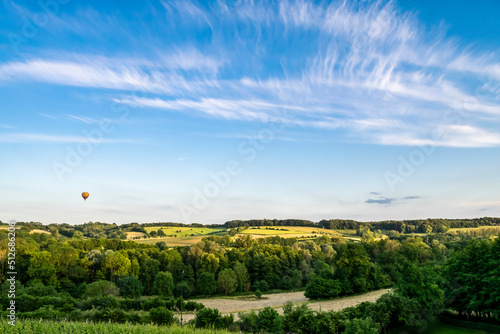 Summer panoramic hilly landscape with fields and forests in Limburg. The hot air balloon flies in the blue sky with white cirrus clouds. photo