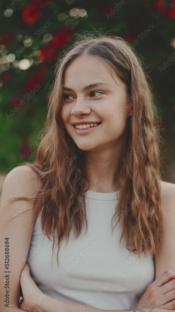 VERTICAL VIDEO: Close-up of smiling beautiful girl with dark blond wavy hair. Pretty girl looking smiling at the camera