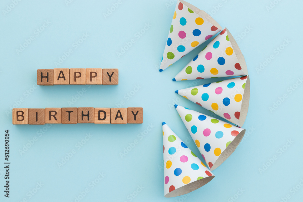 Colorful birthday caps and word happy birthday written wooden cubes isolated on blue