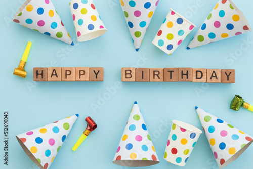 Colorful birthday caps and word happy birthday written wooden cubes isolated on blue