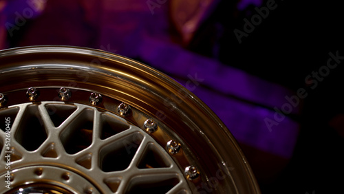 Top down close up view of part of classic three-piece or two-piece wheel rim under yellow light with vibrant purple background, cinematic shot with car parts.