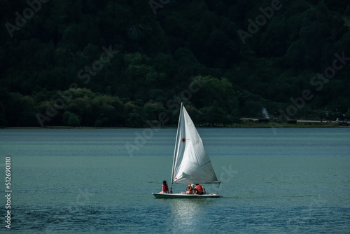 Small sail boat in the Furnas Lake - " Lagoa das Furnas " -, with green vegetation in the background, São Miguel Island in the Azores, Portugal