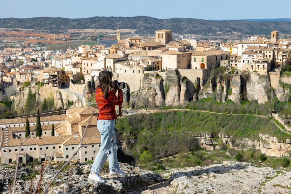 Woman tourist takes pictures of the picturesque houses on the cliff edge of the city of Cuenca. Spain