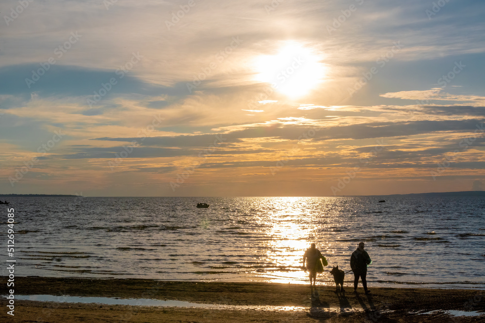 A man, woman, and their dog enjoy a beautifully colourful sunset over Lake Nipissing in North Bay, Ontario.