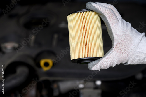  A new car oil filter on the background of the car, in the hand of an automotive mechanic.  photo
