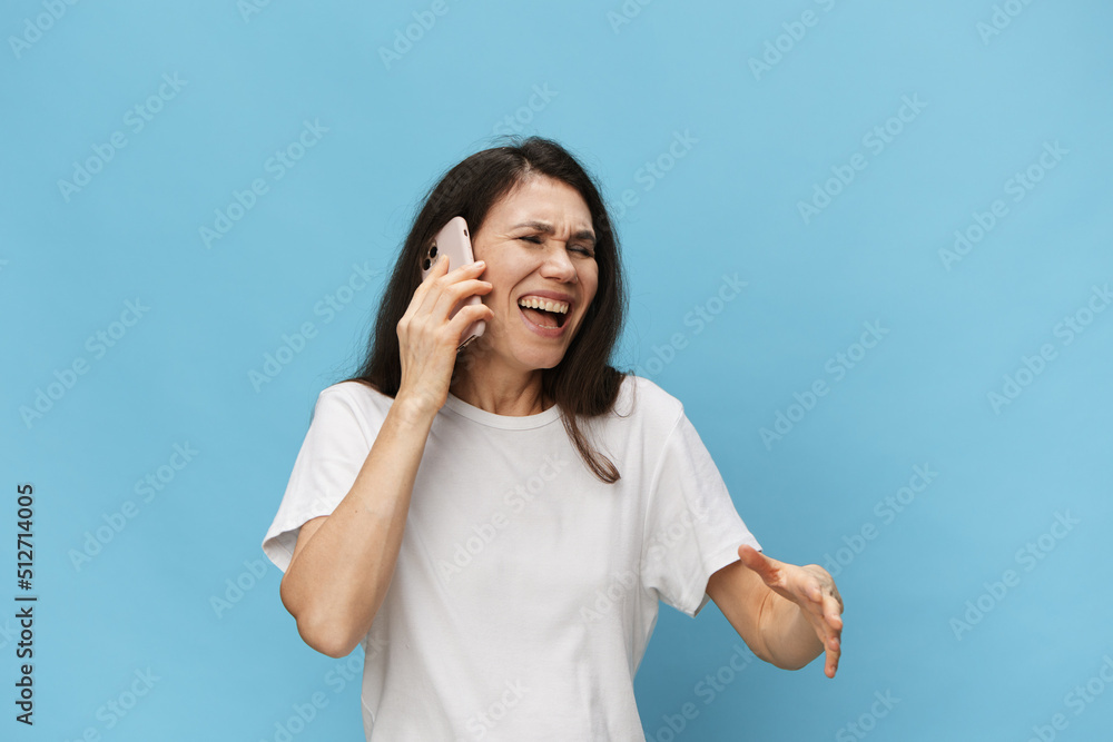 A happy, emotional woman stands on a light blue background and happily laughs while gesturing with her hands during a telephone conversation A happy, emotional woman stands on a light blue background and happily laughs while gesturing with her hands during a telephone conversation
