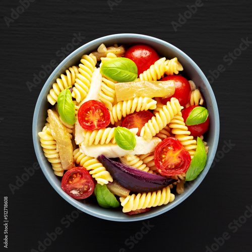 Homemade Fusilli Pasta Salad with Mozzarella and Vegetables in a Bowl on a black surface, top view. Flat lay, overhead, from above.