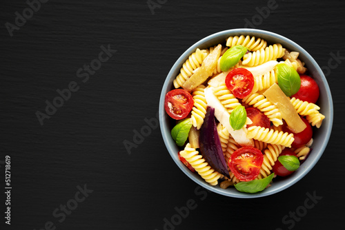 Homemade Fusilli Pasta Salad with Mozzarella and Vegetables in a Bowl on a black surface, top view. Flat lay, overhead, from above. Copy space.