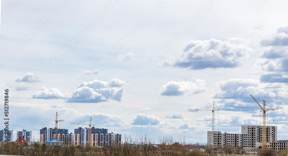 Construction crane and buildings under construction on the background of clouds. Construction of houses in the city or after it.