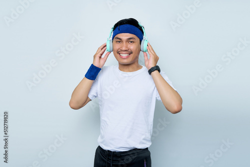 Handsome young asian man sporty fitness trainer instructor in blue headband and white t-shirt. Makes fun Listening to music with headphones isolated over white background