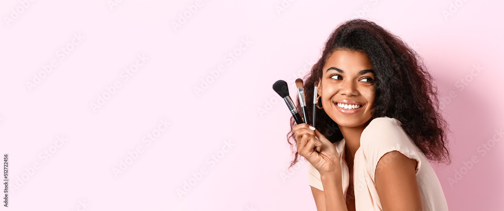 Beautiful young African-American woman with makeup brushes on pink background with space for text - obrazy, fototapety, plakaty 