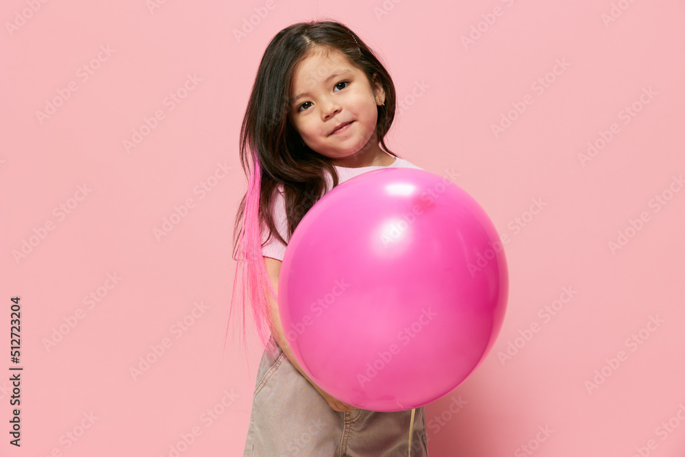 a beautiful little girl of preschool age stands on a pink background and a pink T-shirt and plays with a pink ball, hiding and peeking out from behind it, spreading her arms in different directions a beautiful little girl of preschool age stands on a pink background and a pink T-shirt and plays with a pink ball, hiding and peeking out from behind it, spreading her arms in different directions