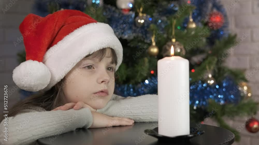 Child atmospheric Christmas with candle. A view of alone child in Santa hat sitting in the atmospheric room for Christmas with burning candle. Child atmospheric Christmas with candle. A view of alone child in Santa hat sitting in the atmospheric room for Christmas with burning candle.