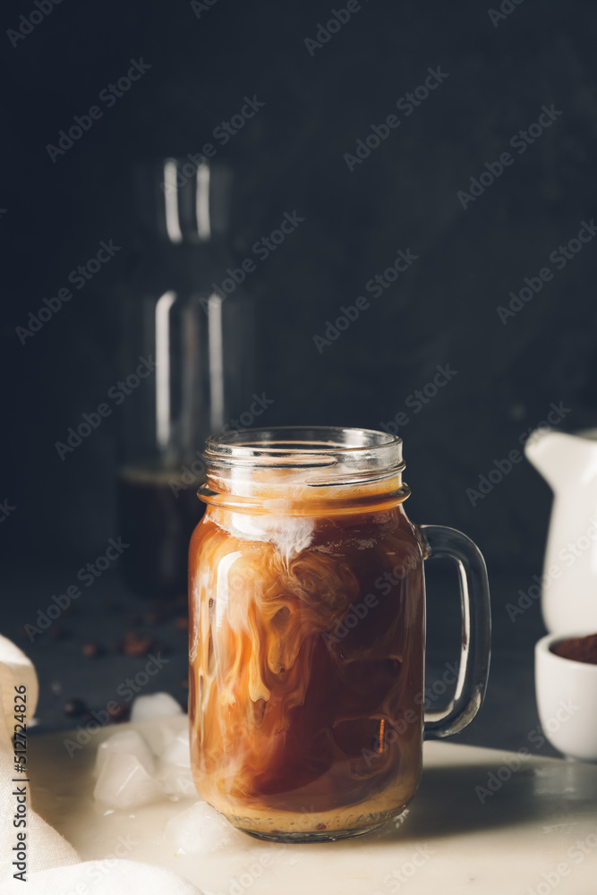 Mason jar with cold brew coffee and milk on board against dark background Mason jar with cold brew coffee and milk on board against dark background