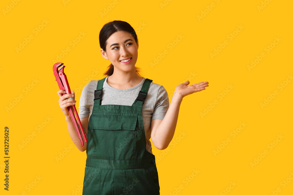 Asian female plumber with pipe wrench on yellow background Asian female plumber with pipe wrench on yellow background
