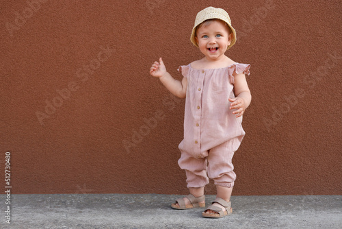 Cute little girl wearing stylish clothes near brown wall outdoors. Space for text photo