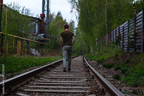 Summer night walk in rain on train tracks of lonely person, view from back, selective or soft focus