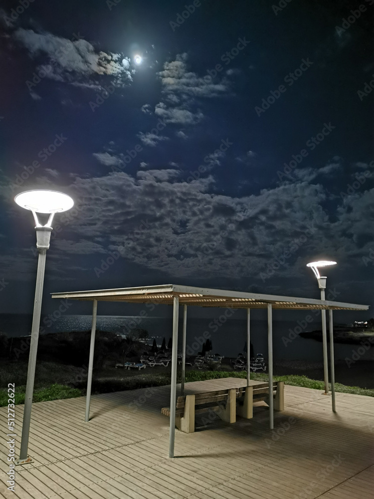 Night Protaras. Benches overlooking the sea under a canopy, illuminated by a lantern, on the promenade near the sea