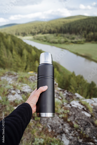 A thermos of steel black color, the equipment of a tourist on a hike, a vacuum bottle retains heat. a hot drink in the woods.