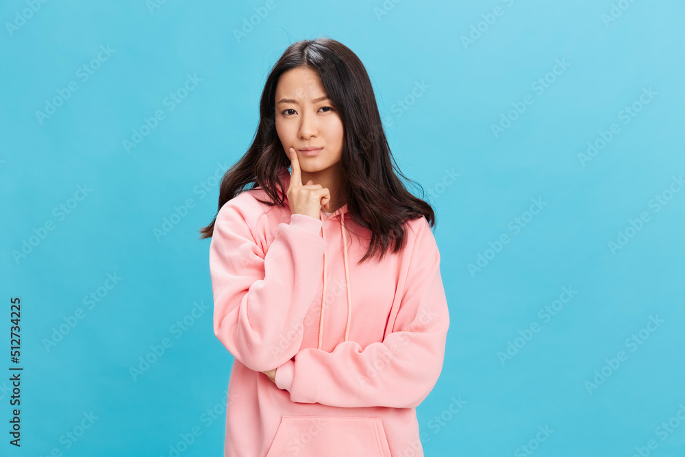 Confused pensive cute Asian student young lady in pink hoodie sweatshirt looks aside posing isolated on over blue studio background. The best offer for ad. People Emotions for Everyday concept Confused pensive cute Asian student young lady in pink hoodie sweatshirt looks aside posing isolated on over blue studio background. The best offer for ad. People Emotions for Everyday concept