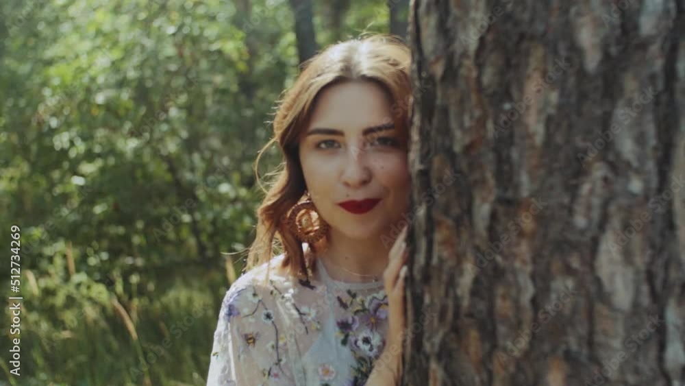 Portrait of beautiful young caucasian woman with red lips posing in the forest near tree bark, handled shot, view through tree branches. Portrait of beautiful young caucasian woman with red lips posing in the forest near tree bark, handled shot, view through tree branches.