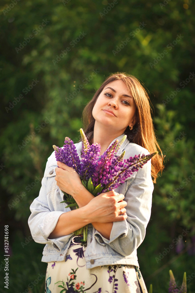 Portrait of a charming girl hugging a bouquet of purple lupins on a background of greenery. Portrait of a charming girl hugging a bouquet of purple lupins on a background of greenery.