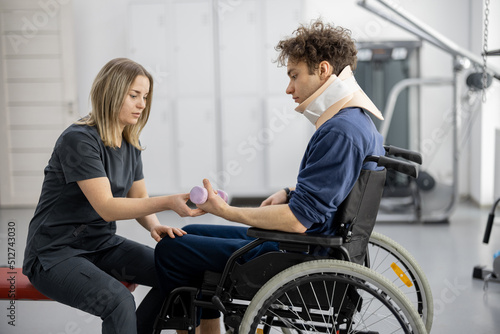 Rehabilitation specialist helps a guy to do exercises for recovery from injury, who is sitting in a wheelchair with a corset around his neck. Concept of physical therapy for people with disabilities photo