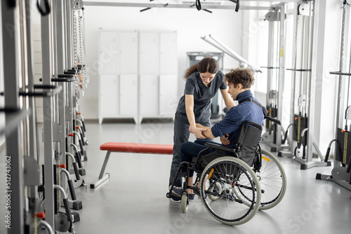 Rehabilitation specialist helps a guy stand out of a wheelchair at rehabilitation center. Concept of physical therapy and support for people with disabilities