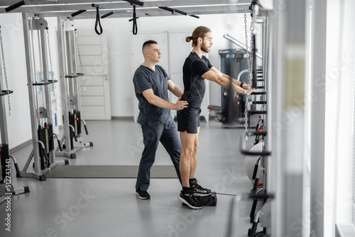 Man doing exercises on decompression simulators with the help of rehabilitation specialist. Concept of physical therapy for health and recovery. Idea of kinesiology in the treatment of back