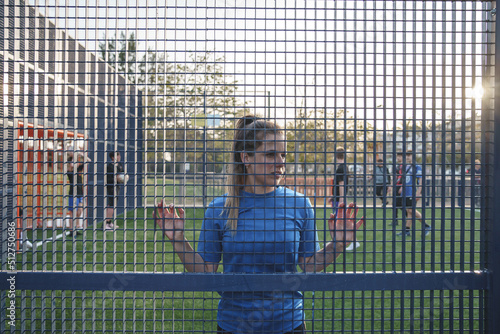 Young female soccer player leaning on net fence on pitch