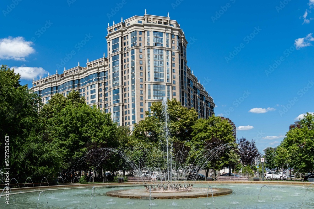 Beautiful cascading fountain against backdrop of residential complex Turgenev. Close-up. Fountain with huge bowl in landscape park. Recreation area in city center. Krasnodar, Russia - June 16, 2022